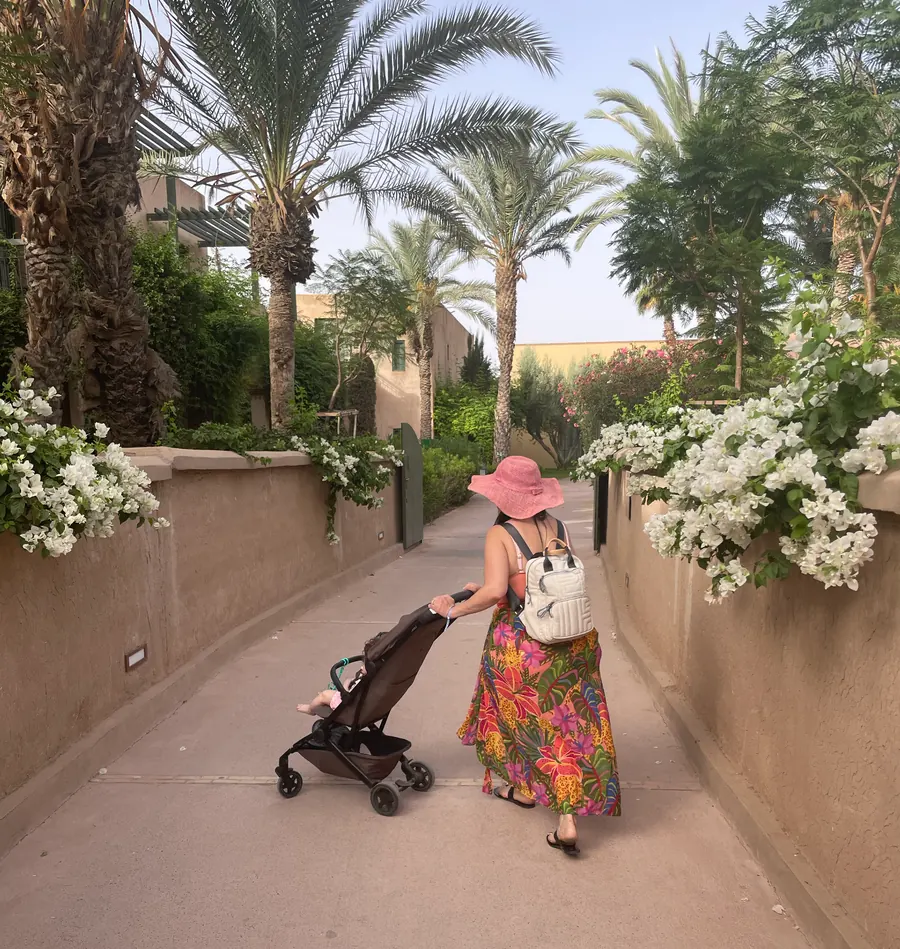 Luana pushing a stroller through a sunlit palm tree pathway - a quiet moment of motherhood in motion